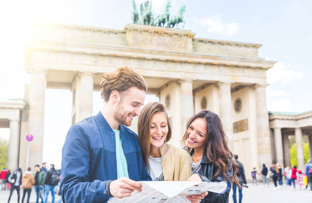 tre unge på studietur til berlin læser et kort foran brandenburger tor