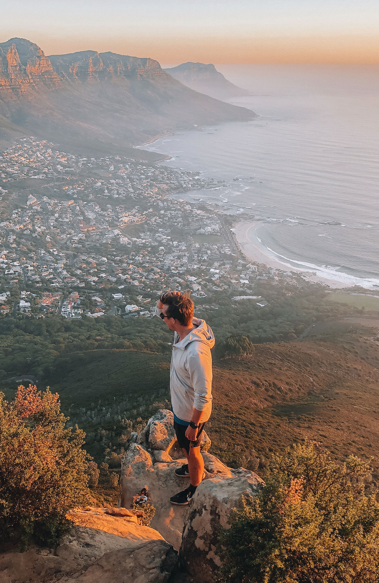 En mandlig rejsende står på en klippe, hvorfra der er udsigt over Cape Towns kystlinje.