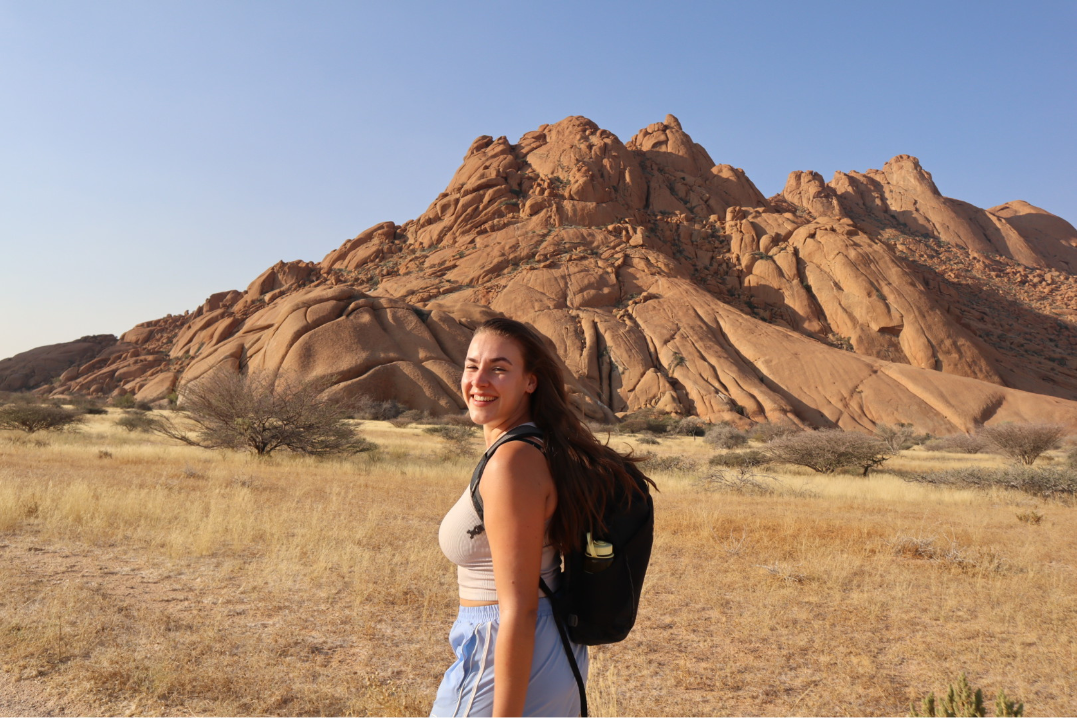Kvindelig rejsende smiler til kameraet, imens hun går foran klipper. 