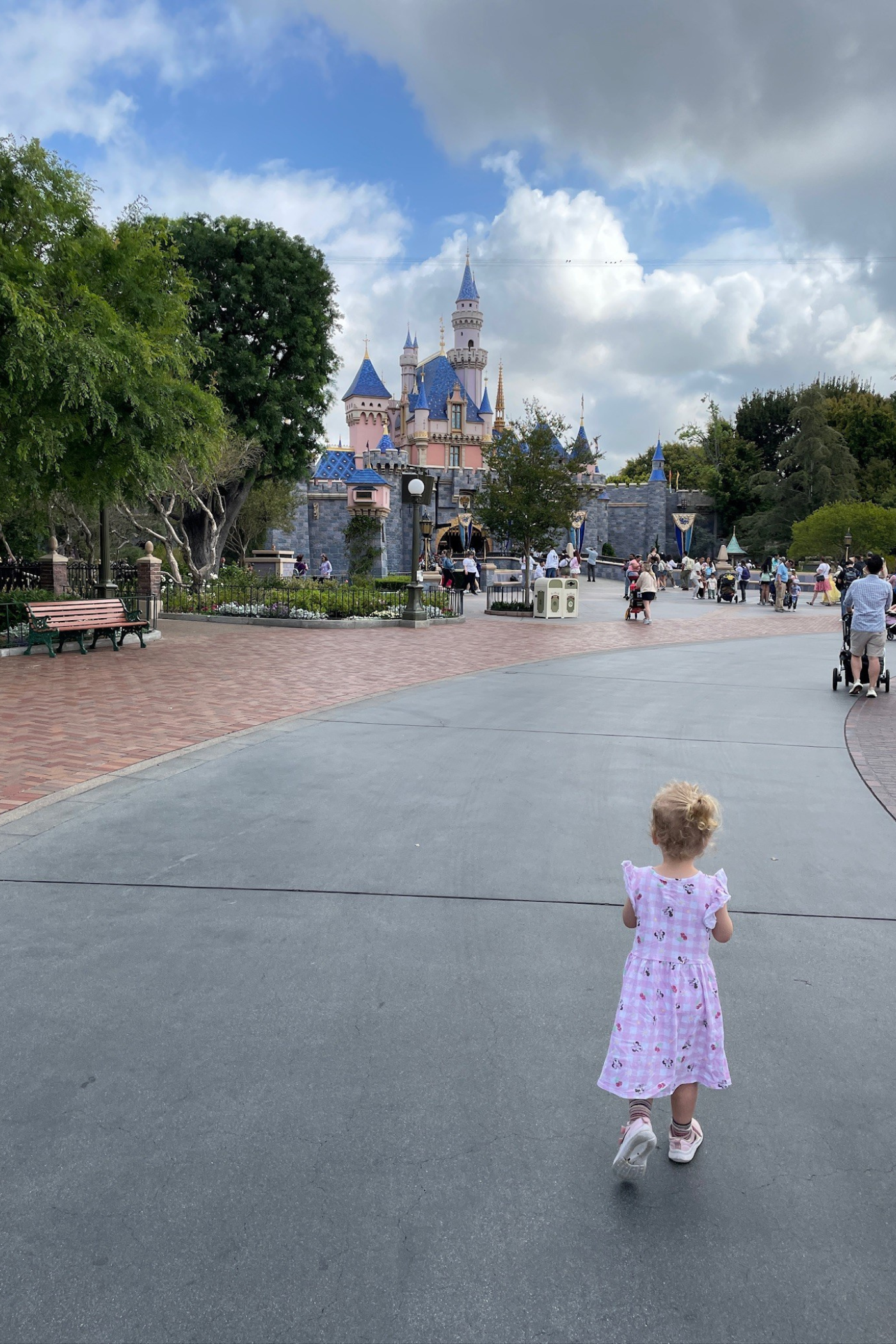 En lille pige i lyserød kjole går på fortovet - foran hende ses Disneyland. 