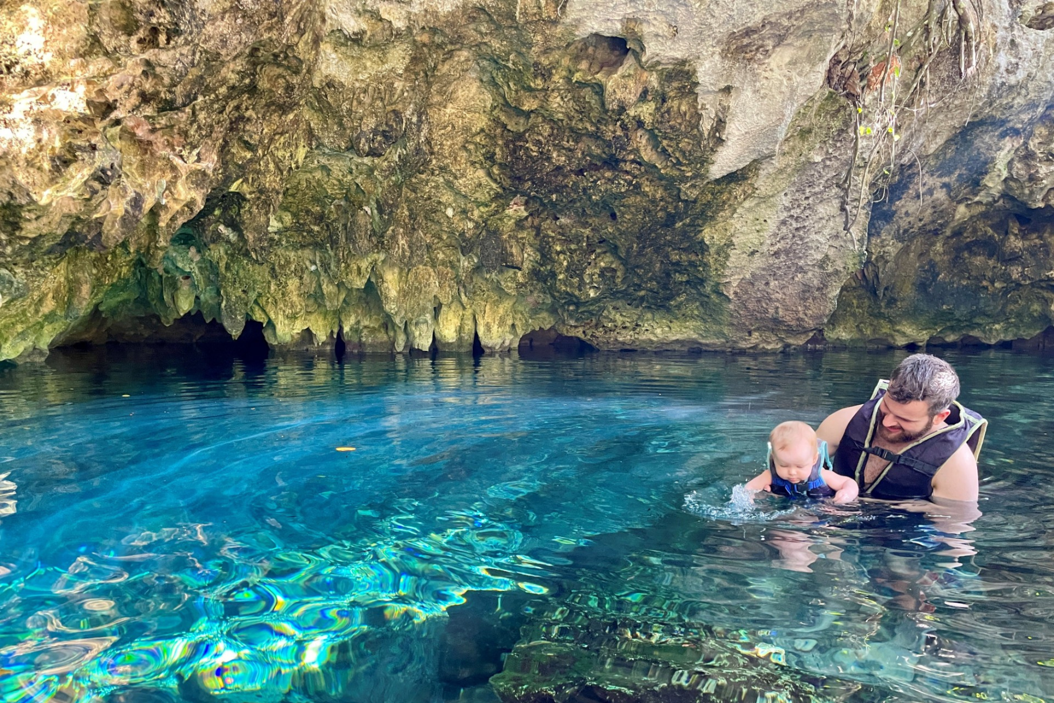 En far med en baby svømmer i en cenote i Mexico. 
