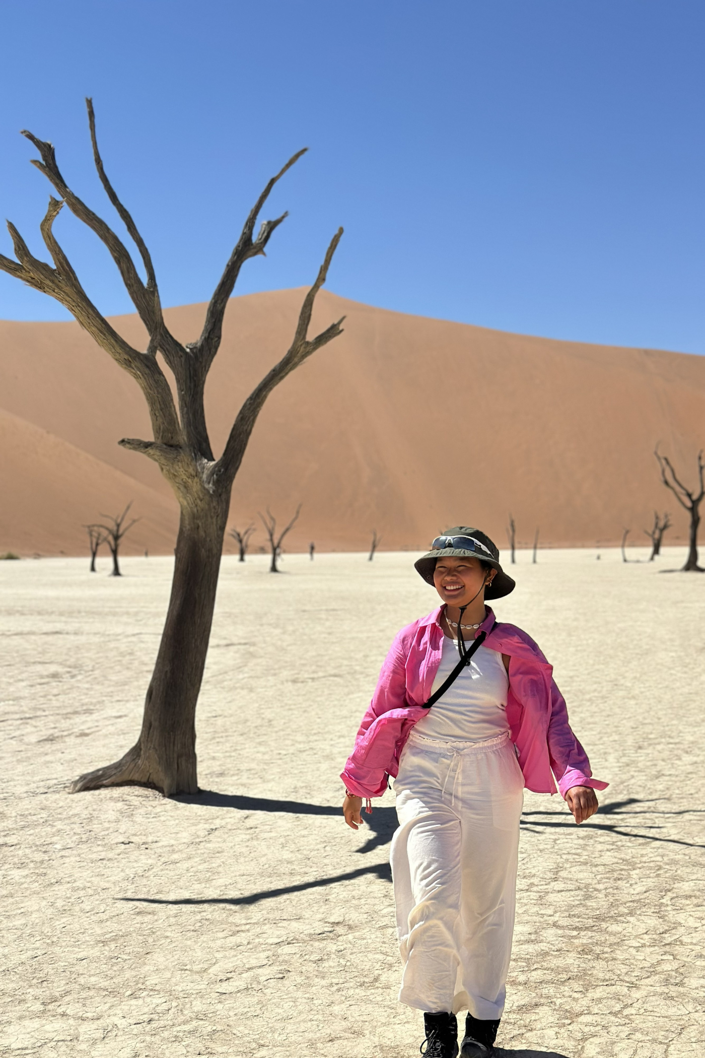 Kvindelig rejsende går smilende rundt i ørkenen ved DeadVlei i Namibia. 