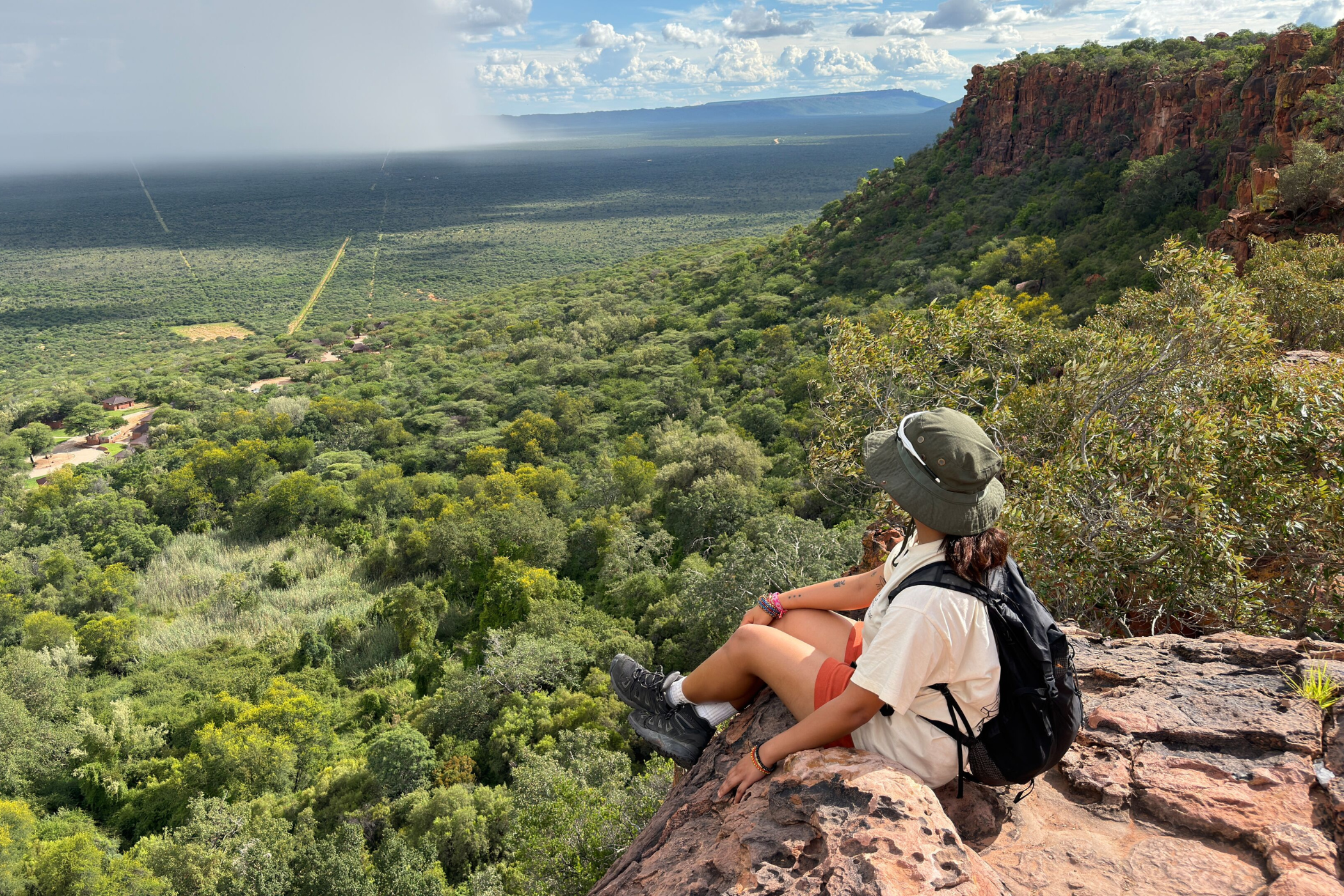 Rejsende sidder på en klippe og kigger ud over et grønt, frodigt landskab. 
