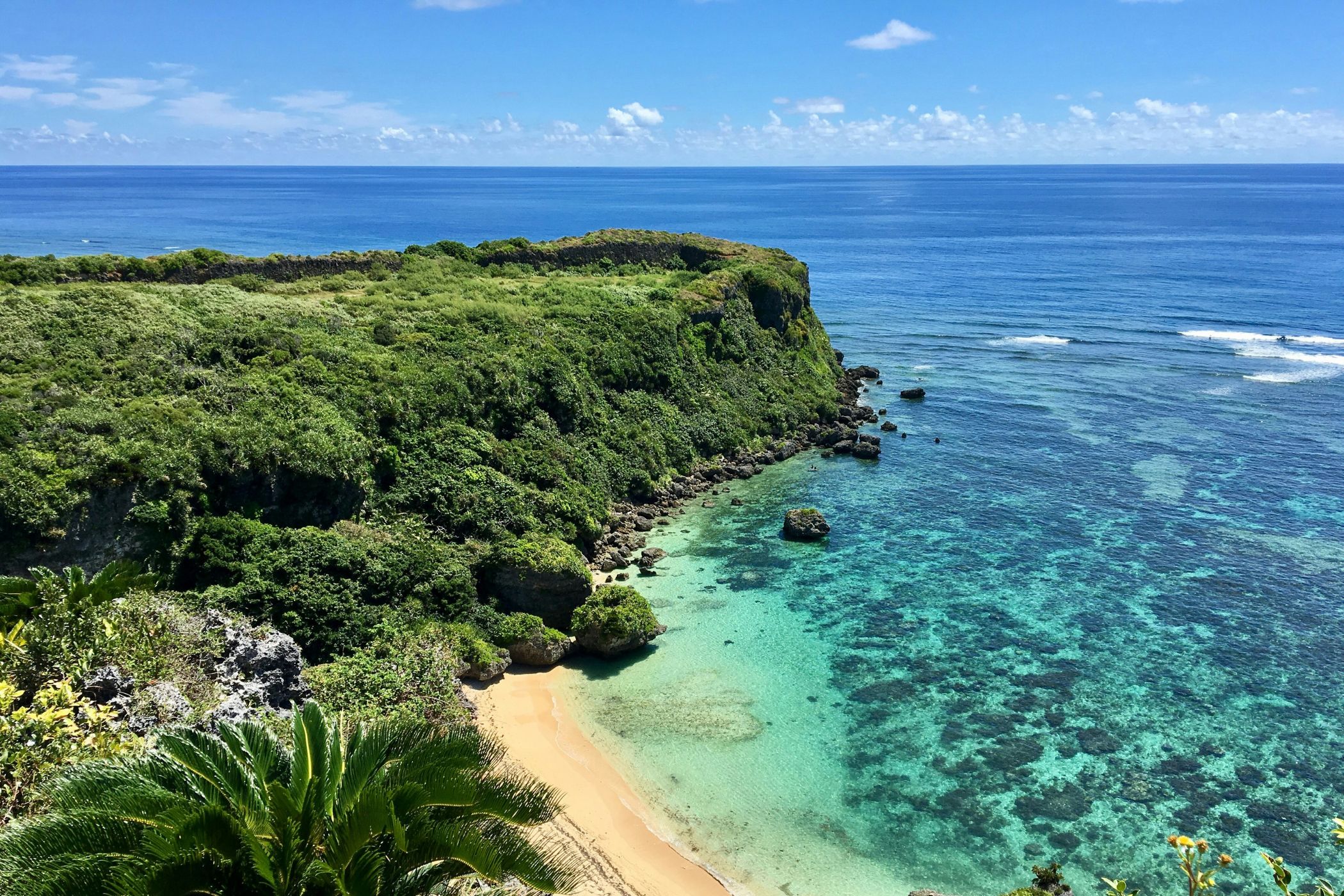 Landskabsbillede fra Okinawa i Japan. Man ser grøn vegetation, der spreder sig ud over en hvid sandstrand og turkisblåt vand.