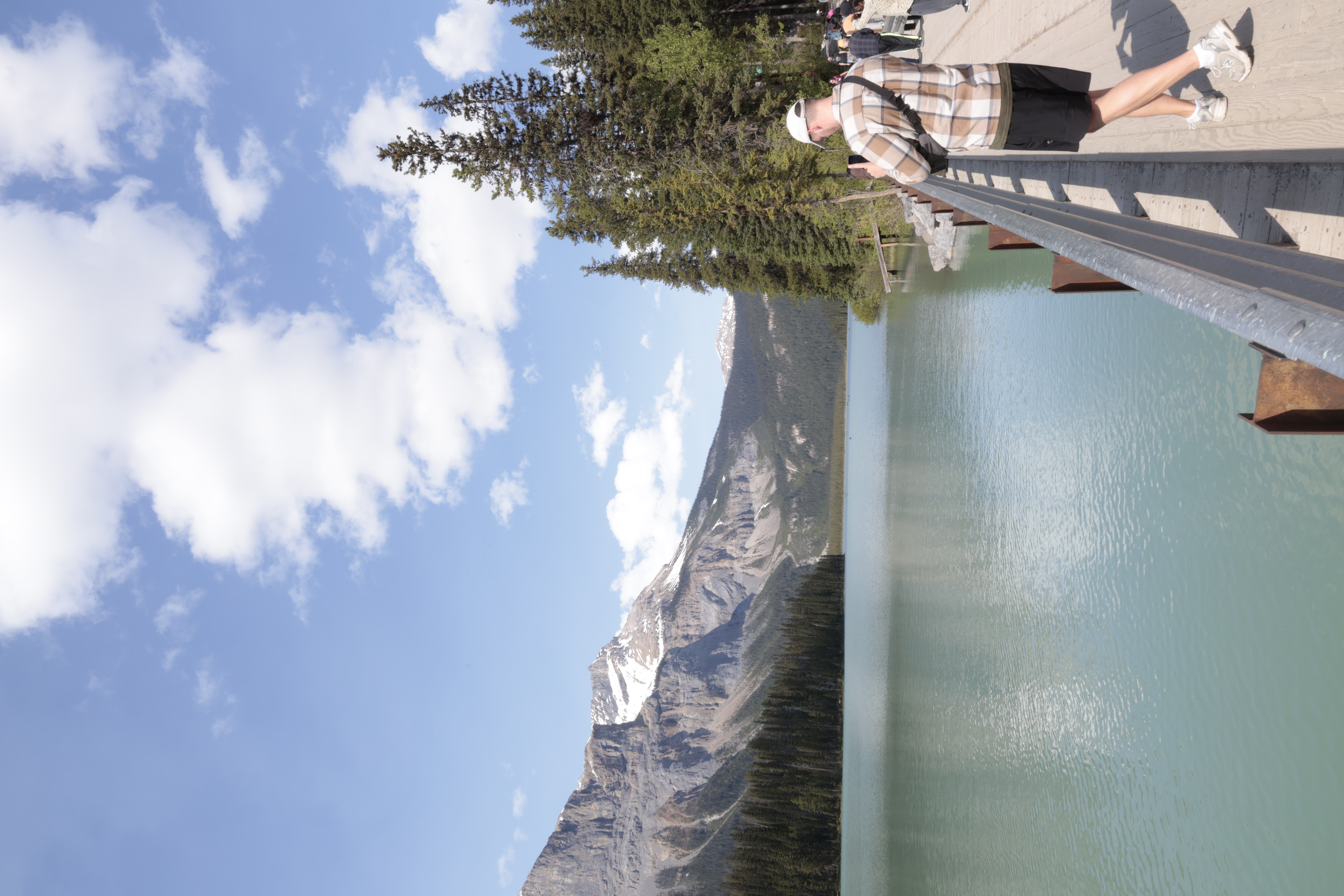 Mand med ryggen til tager et billede ud over en sø med bjerge i baggrunden. 