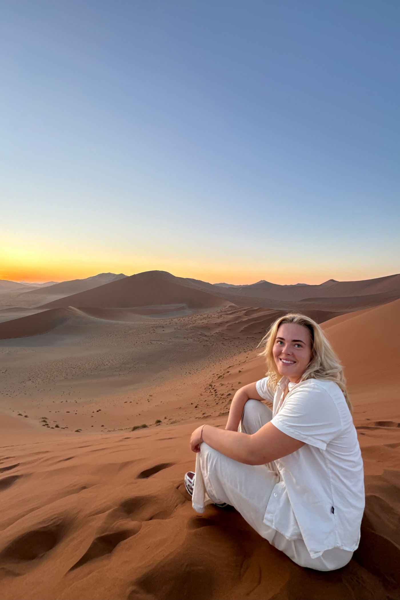 Kvindelig rejsende sidder i ørkenen i Namibia. Hun smiler til kameraet.