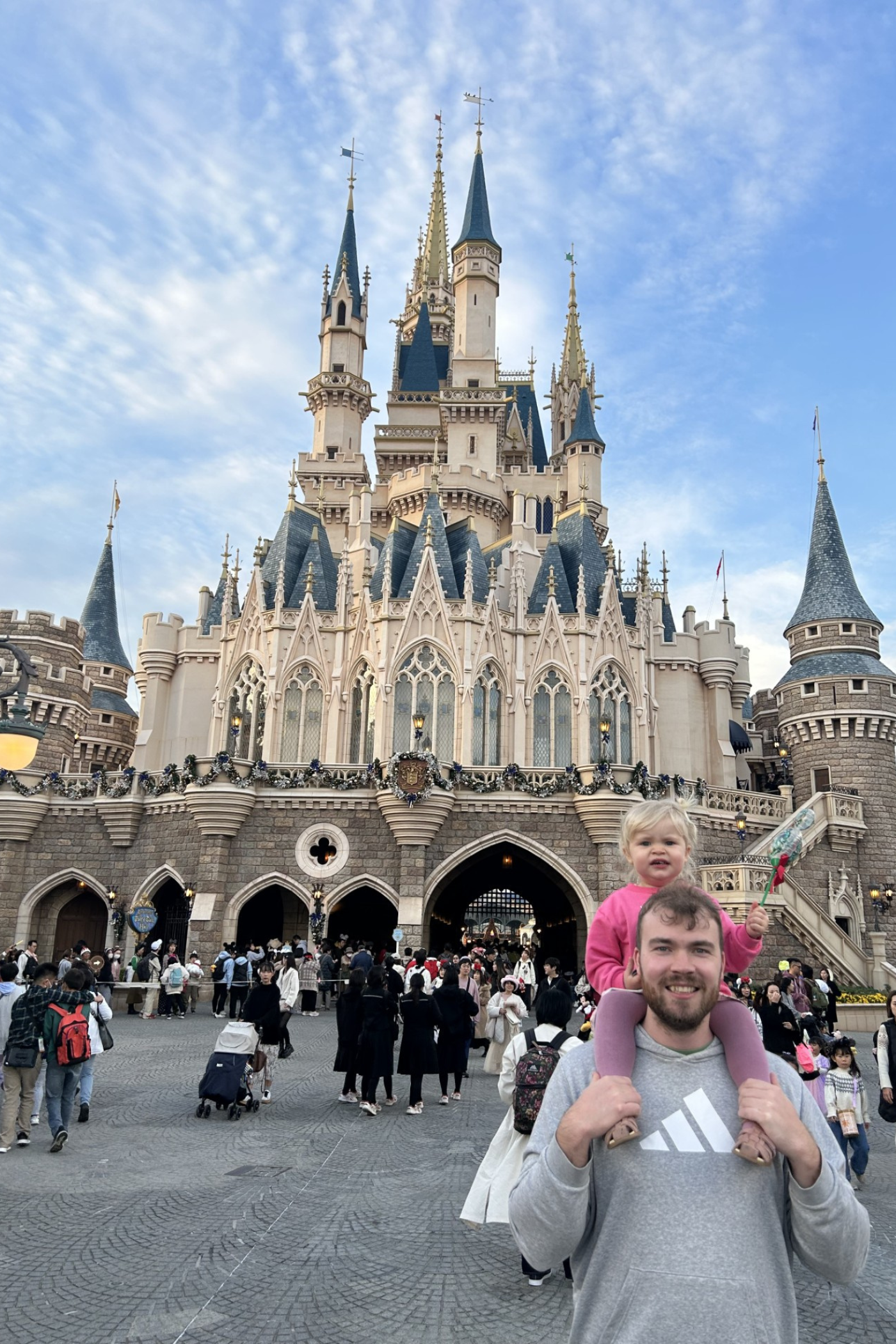 Mand med et lille barn på skuldrene foran et slot i Disneyland i Tokyo. 
