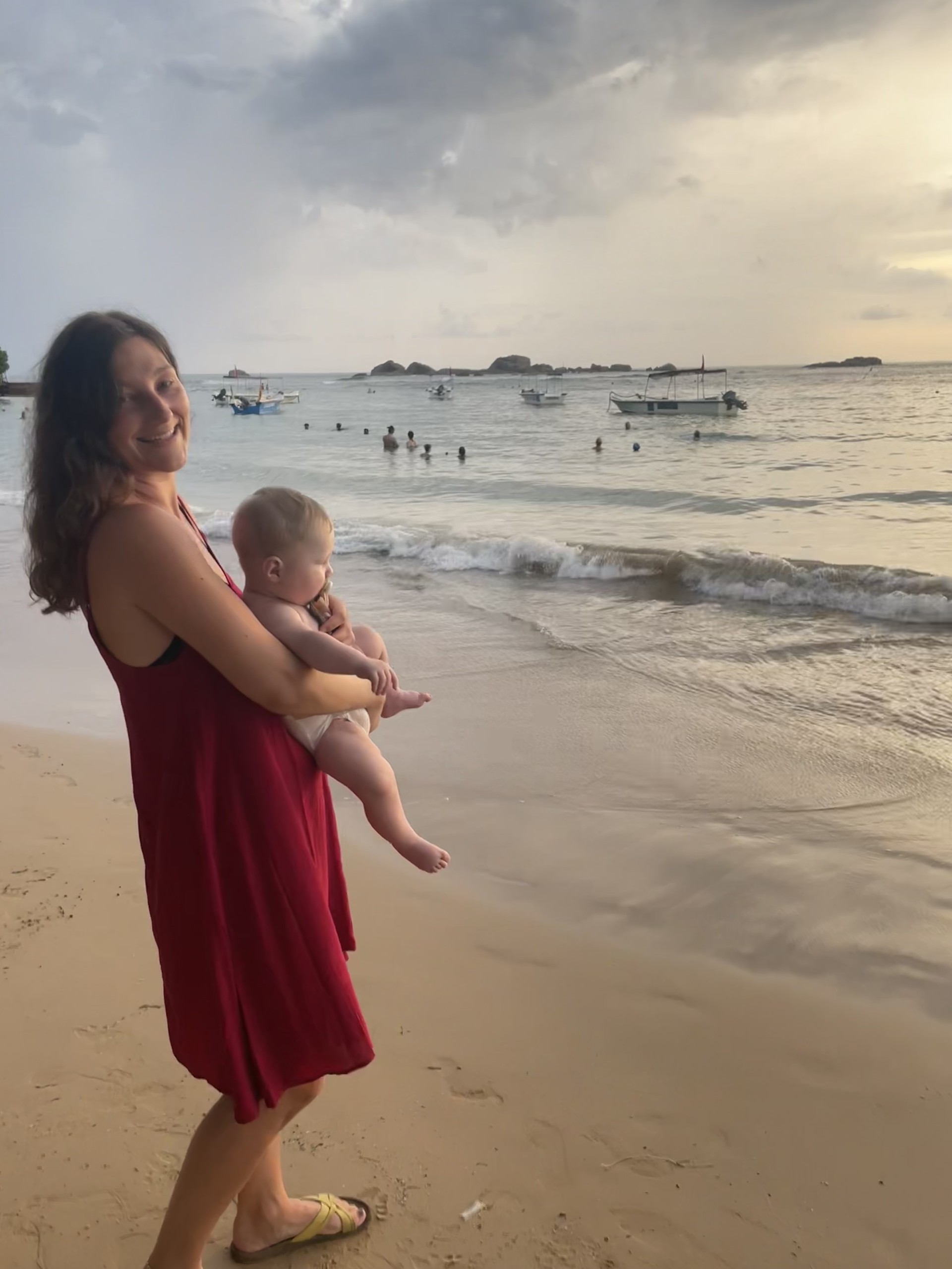 Mor med et lille barn på armen på en gylden sandstrand. 