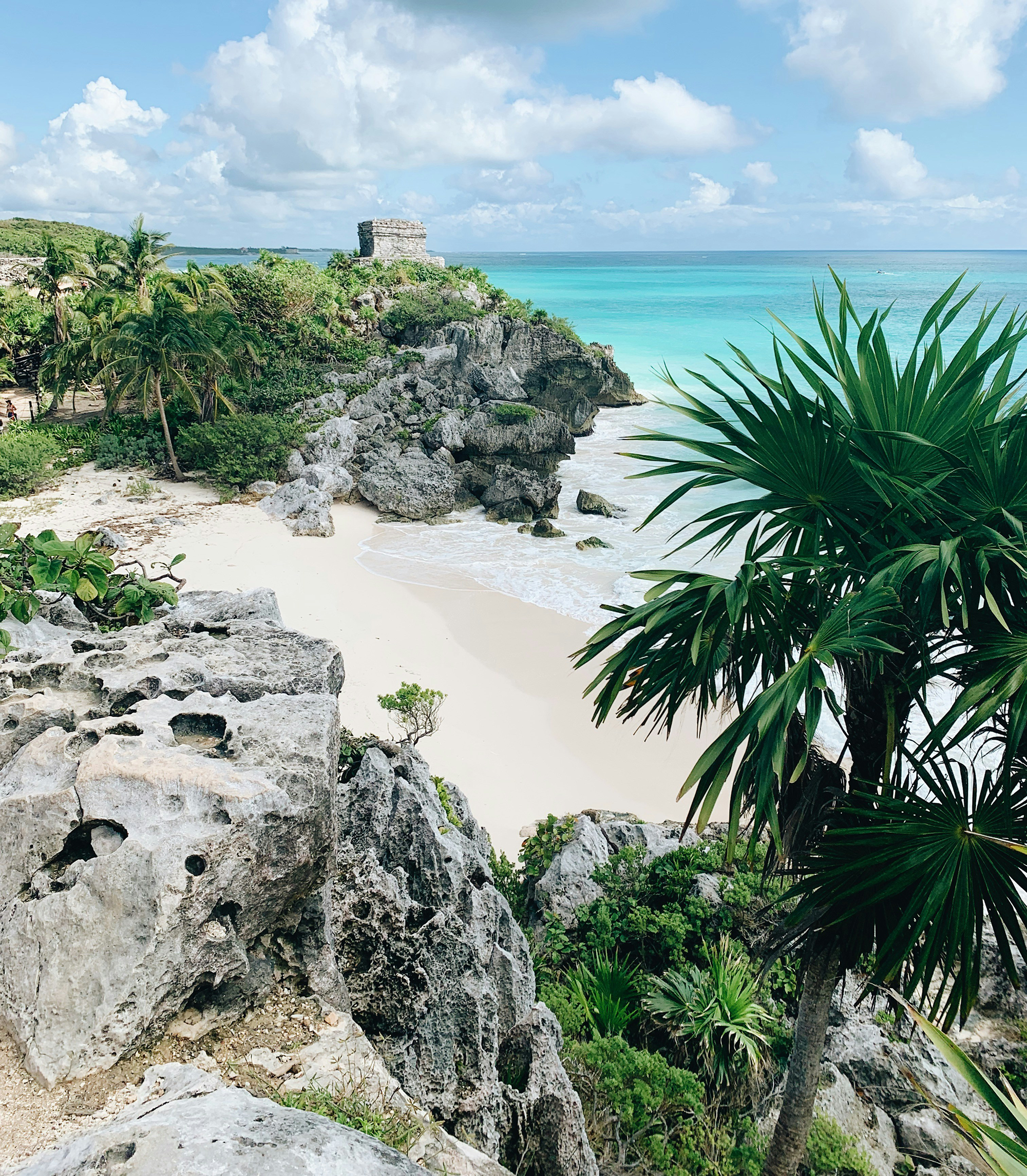 Strand i Mexico med klipper langs vandkanten og en ruin i baggrunden. 